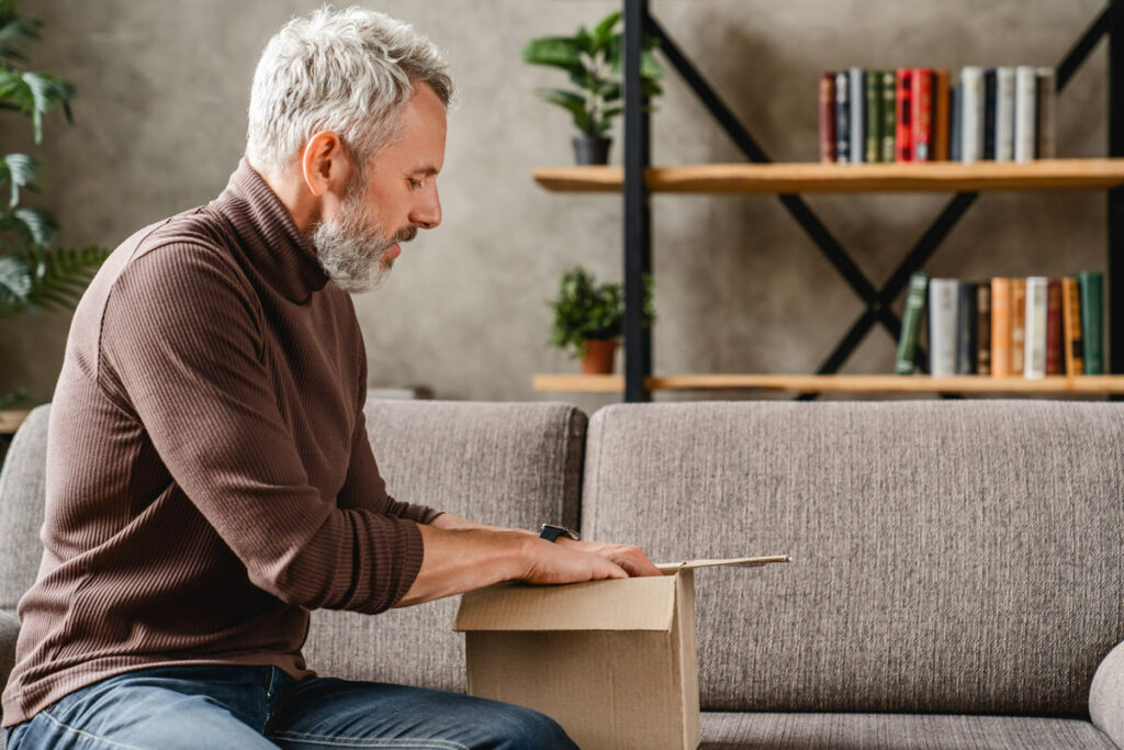 Atlas Senior Living | Senior man downsizing sitting on the couch with a small cardboard box