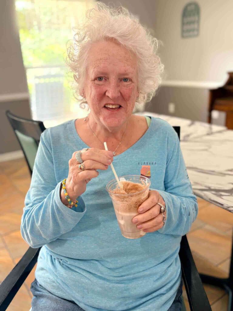 Older woman smiling while enjoying a drink during a relaxed activity at Madison Heights & Kelley Place in Enterprise, AL.