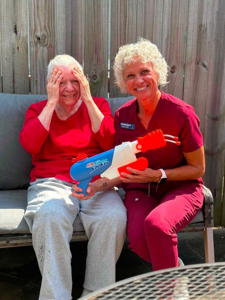 Older woman smiling outdoors with a caregiver during a playful activity at Madison Heights & Kelley Place in Enterprise, AL.