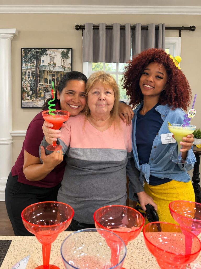 Three women smiling together with margaritas during a social gathering at Madison at Ocoee