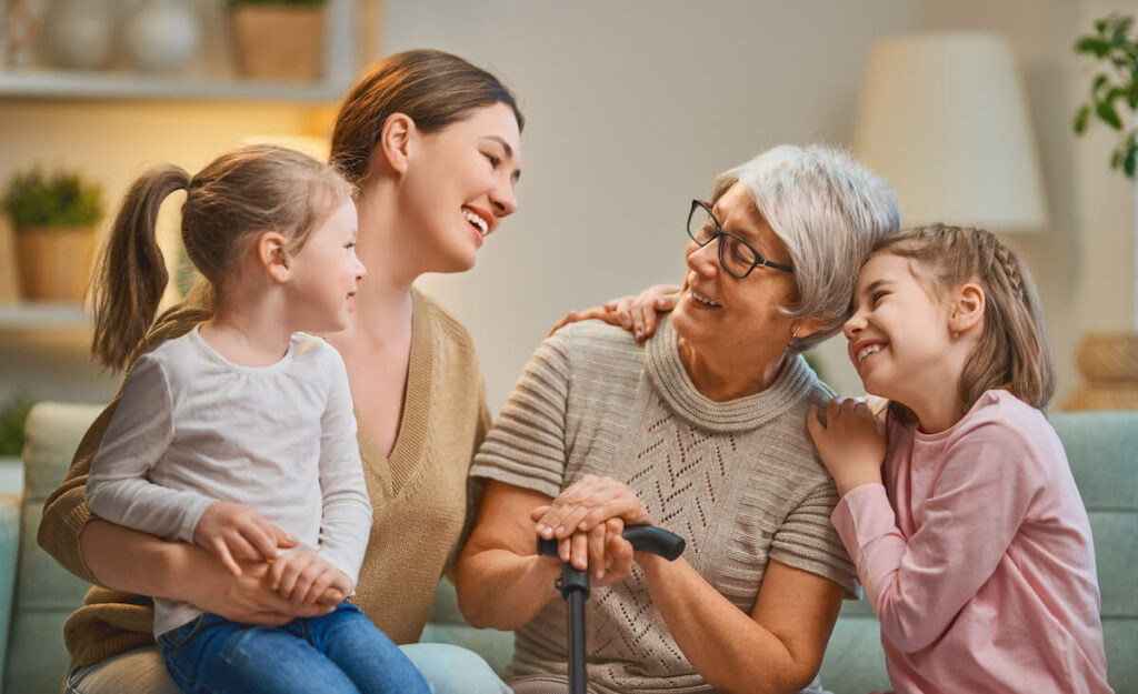 The Goldton at St. Petersburg | Happy senior woman and her family smiling, while sitting on the couch