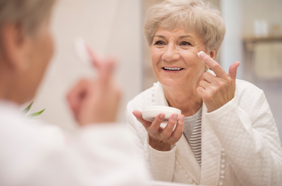 Older woman applying facial moisturizer as part of a daily skin care routine for healthy, hydrated skin after 70.