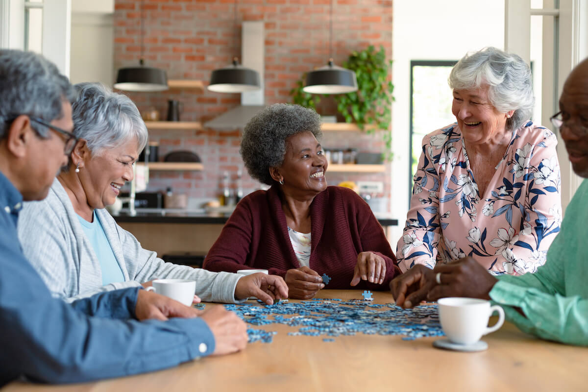 Atlas Senior Living | Group of seniors socializing, while doing a puzzle