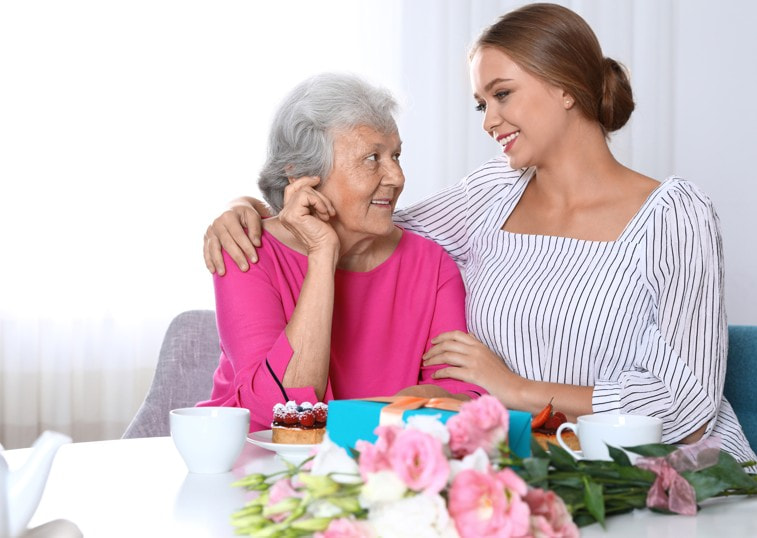 Before planning the visit, think of Mother’s Day in Memory Care as a comfort design moment. Instead of asking, “What should we do for Mom?” try asking: What does her nervous system recognize as safe? What kind of moment would feel familiar without overwhelming her? What can we bring that speaks through emotion, not explanation? This matters because dementia can change memory, language, and attention, but emotional responses, sensory cues, and familiar rhythms can still create meaningful connection. Person-centered dementia care focuses on the individual’s preferences, life history, emotions, and daily comfort, which makes the “small details” of a visit much more important than the size of the celebration (Marulappa et al., 2022). A helpful way to plan the day is to build it around one gentle anchor: A sound she knows A favorite song, hymn, artist, or family recording can create a moment of recognition even when conversation feels difficult. Personalized audio cues have been studied as a way to support well-being and connection in dementia care (Edwards et al., 2024). A texture she can hold A soft scarf, a familiar blanket, a family photo book, or a small object from her past can give the visit something physical and calming to return to. A taste connected to memory A favorite dessert, tea, fruit, or holiday treat can turn the visit into a sensory experience instead of a performance. A sentence that does not test her Instead of “Do you remember when…?” try: “Mom, I always loved this photo of us.” “This song makes me think of you.” “I’m happy to be here with you today.” The goal is not to make her prove what she remembers. The goal is to let her feel that she is loved, safe, and included. A meaningful Mother’s Day in Memory Care may be shorter, quieter, and simpler than past celebrations. That does not make it less valuable. For families navigating dementia, the most loving choice is often the one that reduces pressure: fewer questions, fewer expectations, more presence. Because sometimes the best celebration is not a big event. It is Mom hearing a familiar song. Mother’s Day with Mom in Memory Care What Truly Matters