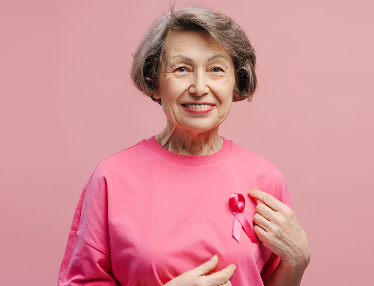 Senior woman wearing a pink shirt and breast cancer awareness ribbon, highlighting breast health after 70, healthy aging, and breast cancer prevention.
